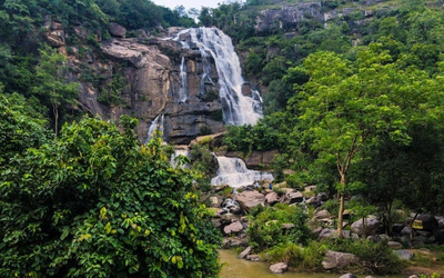 A large, multi-tiered waterfall flowing over dark rock faces, surrounded by dense green foliage